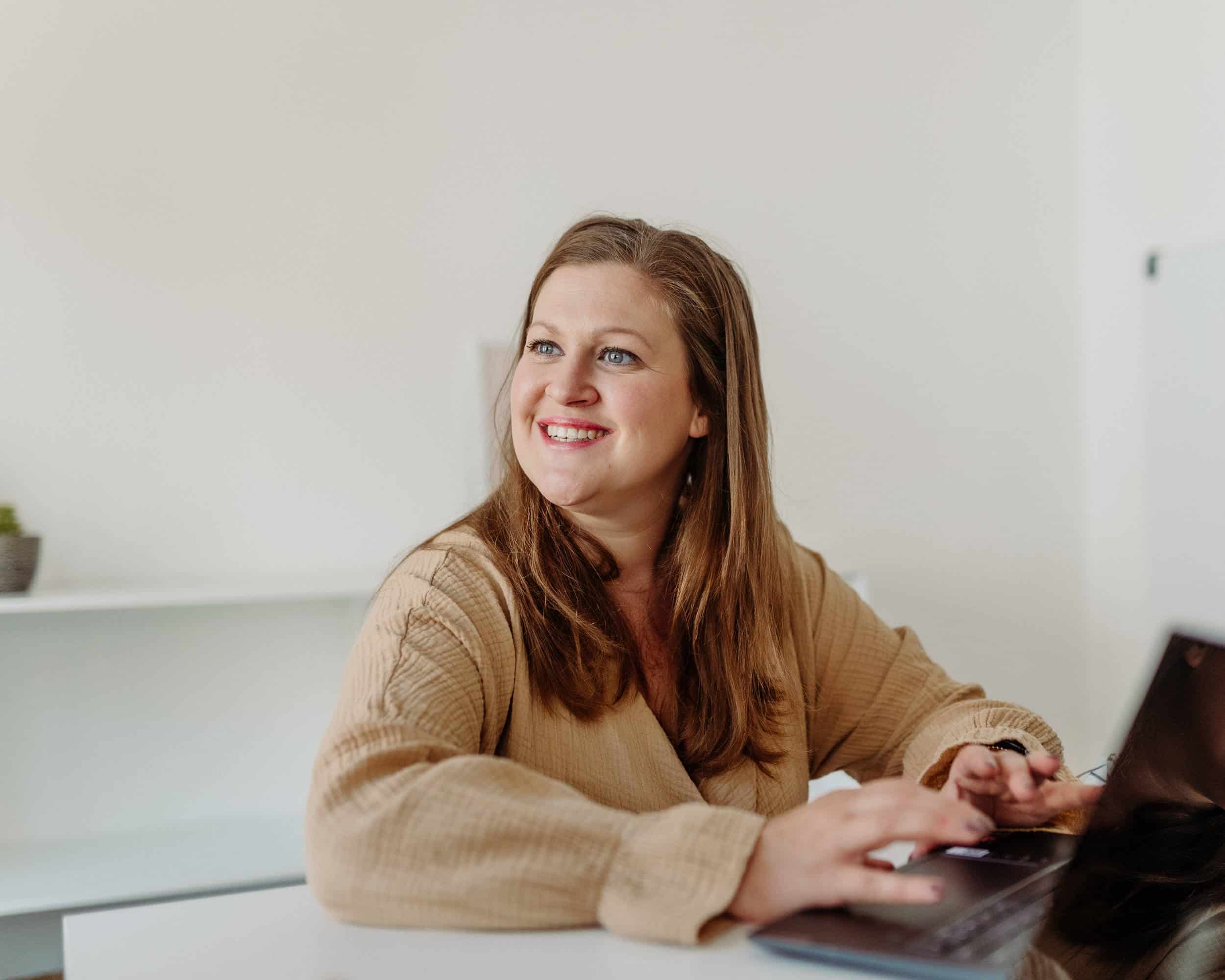 Karin sitzt in einem modernen Meeting-Raum an ihrem Laptop. Sie lächelt ihren Kollegen an.